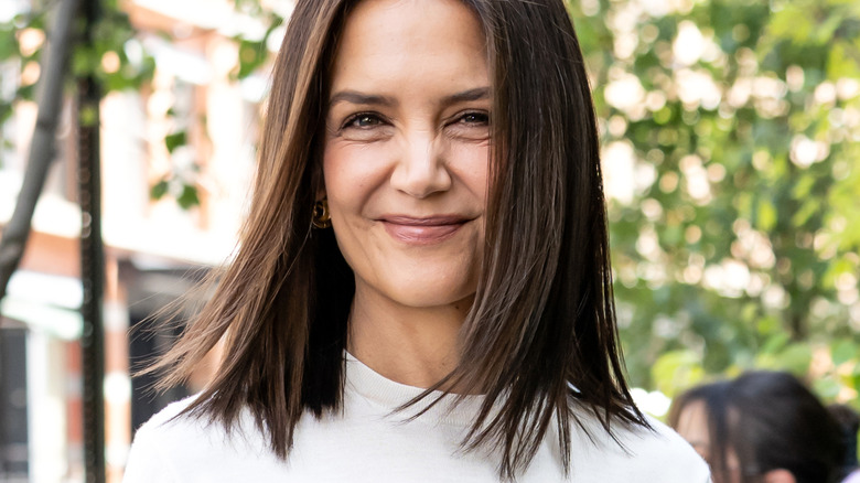 Katie Holmes smiles directly into the camera against a leafy backdrop