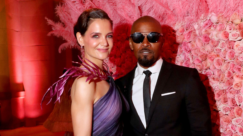 Katie Holmes and Jamie Foxx posing for a photo against a fancy floral backdrop.