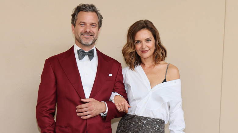 Joshua Jackson and Katie Holmes smiling arm in arm at a red carpet event.