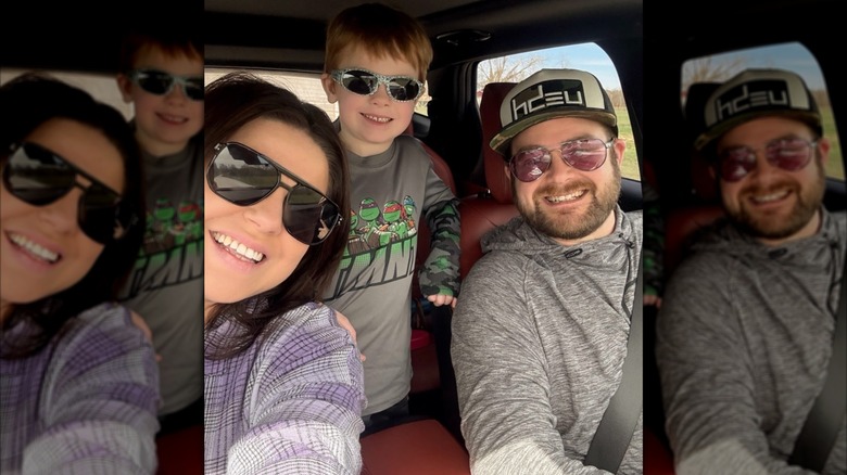 Amy poses with her husband and their young son in a car.