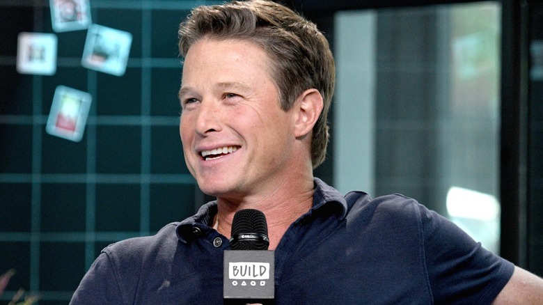 A smiling Billy Bush holding mic