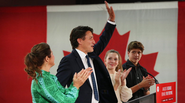Justin Trudeau raising his hand in front of a Canadian flag while his wife and children clap