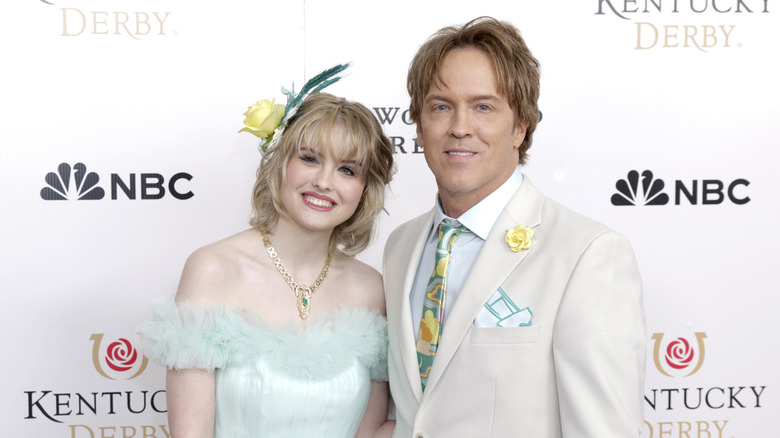 Dannnielynn in light blue gown and green and yellow fascinator standing with dad
