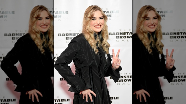 Dannielynn with long hair smiling in long sleeved black dress making peace sign