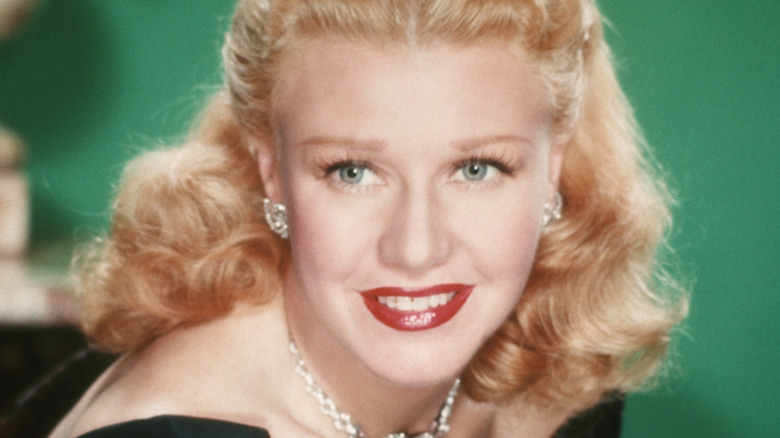 A colorized portrait of Ginger Rogers smiling with silver jewelry and red lipstick.