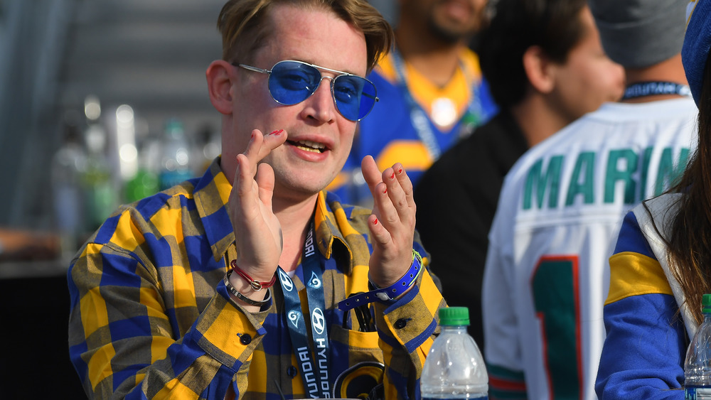 Macaulay Culkin clapping, wearing blue sunglasses