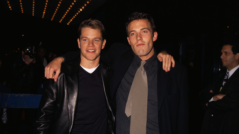 Matt Damon in leather jacket and Ben Affleck in formals with arms around each other