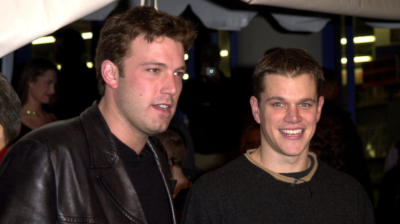 Ben Affleck in a leather jacket as Matt Damon smiles into the camera