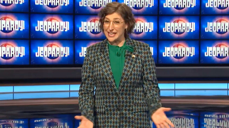 Mayim Bialik standing in front of the Jeopardy! monitors in a promo