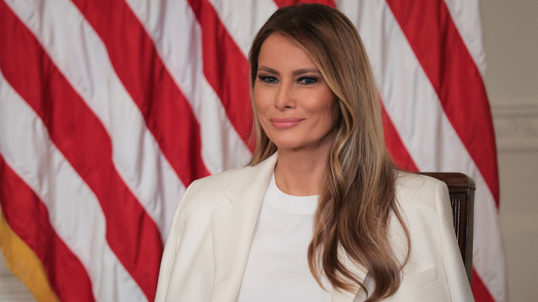 Melania Trump smiling in a white blazer and white T-shirt