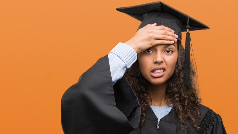 woman in graduation cap holding head and looking confused