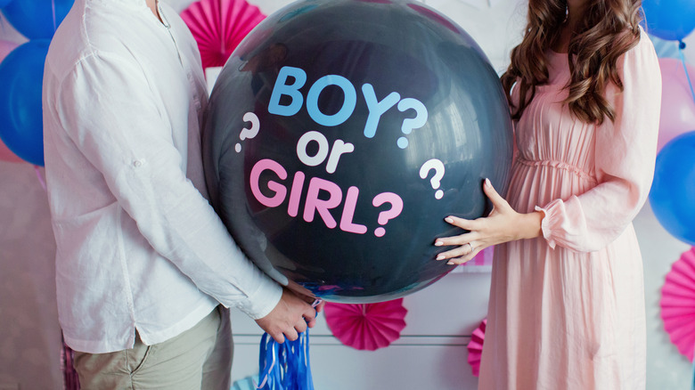 man and woman holding gender reveal balloon