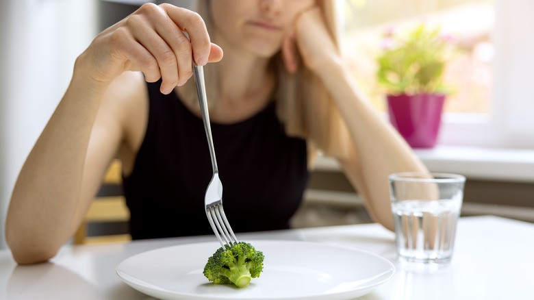 Woman pokes a single piece of broccoli with a fork