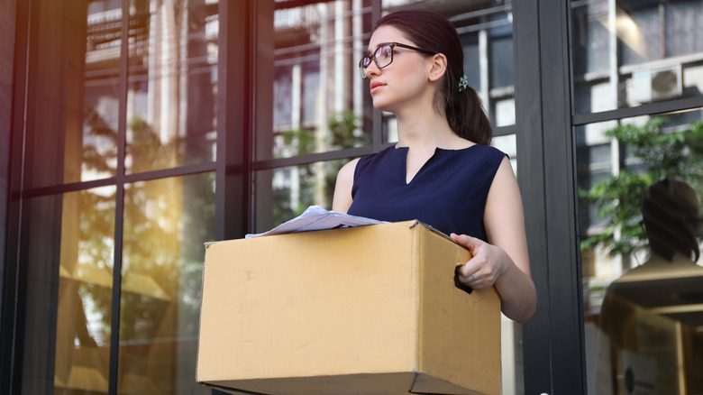 Woman with glasses carrying box out of work