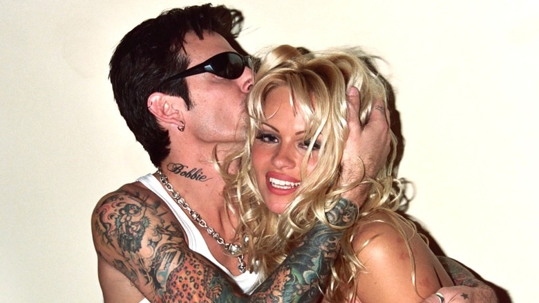 Tommy Lee in sunglasses with his arm around Pamela Anderson as he kisses her on the head.