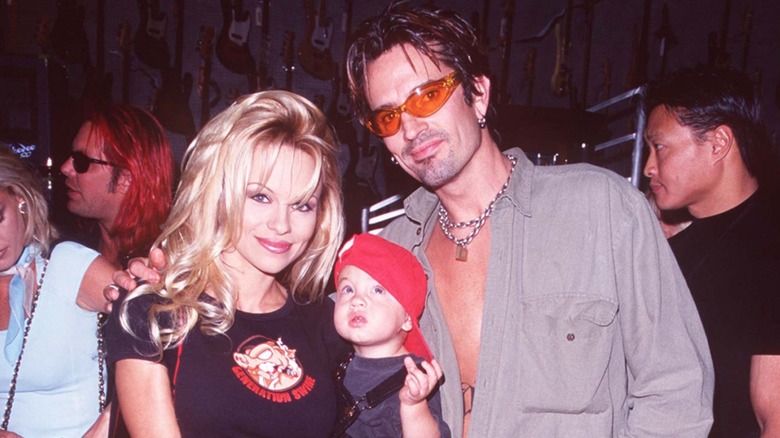 Pamela Anderson holding her son, with Tommy Lee in orange sunglasses.