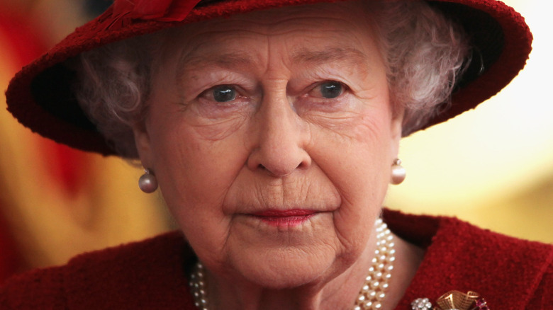 Queen Elizabeth looking to the side wearing red hat