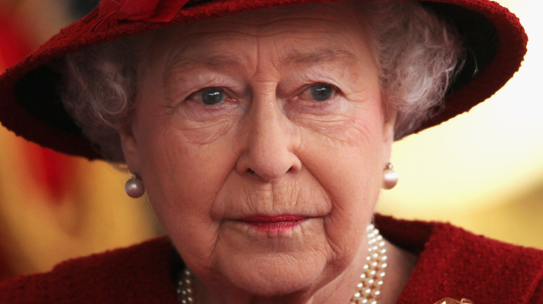 Queen Elizabeth wearing a red hat and pearls