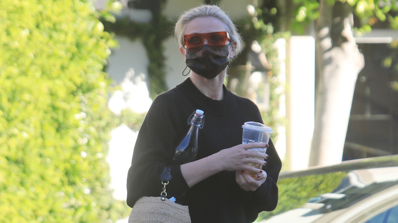 Cameron Diaz photographed on street wearing sunglasses, a face mask, and carrying a water bottle, an iced drink, and handbag