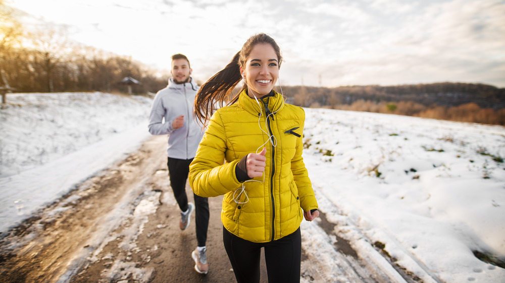 Woman in yellow jacket and man running in the snow