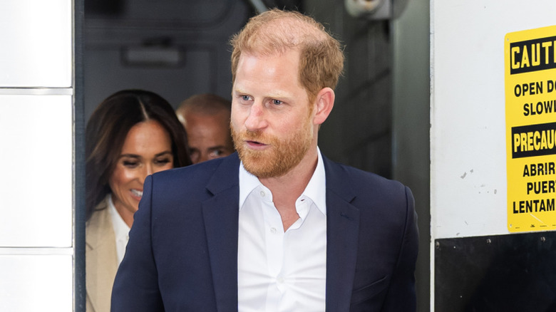 Prince Harry exiting a building with Meghan Markle behind him