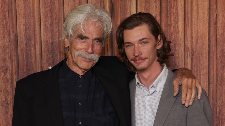 Sam Elliott with his arm around Jacob Lofland on a wood-paneled Landman red carpet.