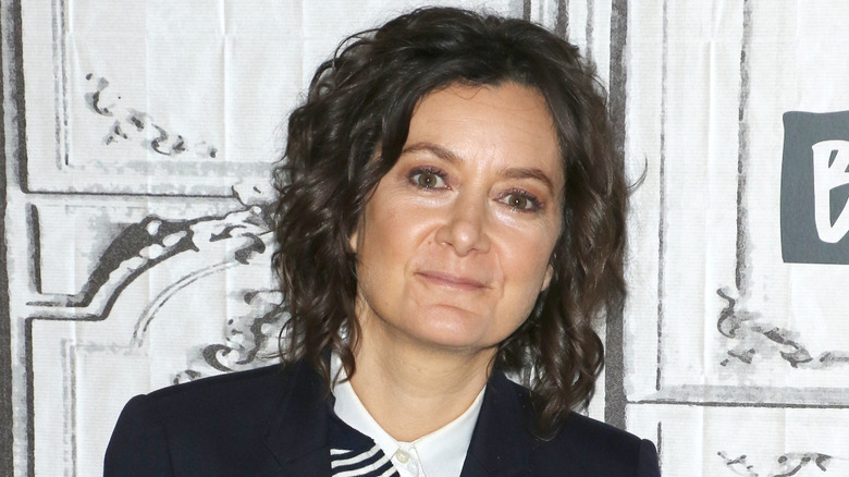 Sara Gilbert posing with a neutral expression in a black blazer with a monochrome patterned shirt underneath