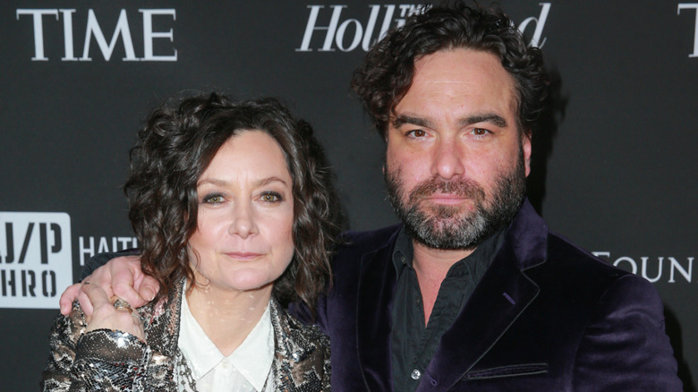 Johnny Galecki in a suit posing with his arm around Sara Gilbert in a sparkly jacket
