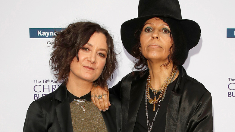 Linda Perry posing with her hand on Sara Gilbert's shoulder in a big black hat