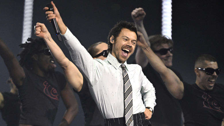 Harry Styles sporting a wide grin as he performs a dance on stage