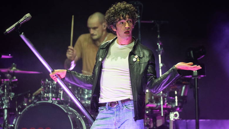 Matty Healy elaborately shrugging while performing on stage