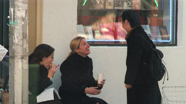 Carolyn Bessette-Kennedy holding to-go coffee cup smiling with friends outside bookshop