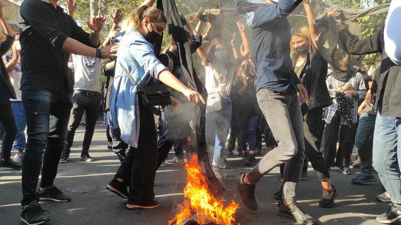 Woman burning headscarf while protestors dance