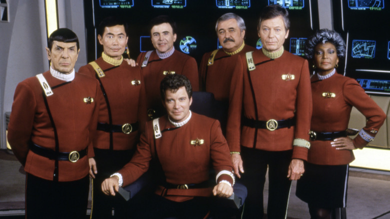 Leonard Nimoy, George Takei, Walter Koenig, James Doohan, DeForest Kelley, Nichelle Nichols standing in front of a seated William Shatner on the set of 'Star Trek'