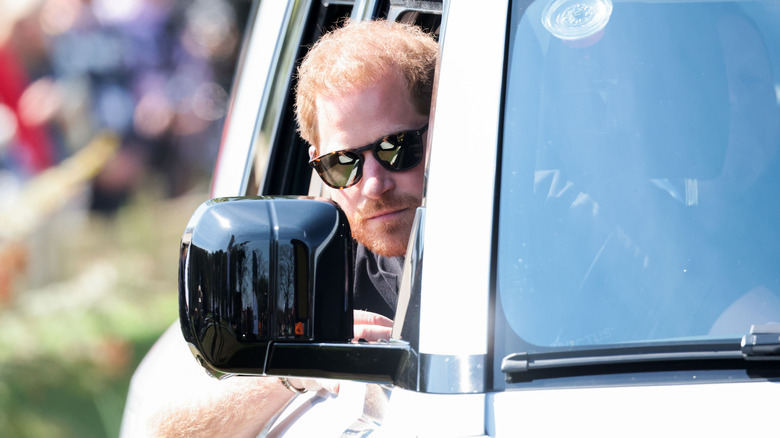 Prince Harry peeking from behind the wheel, wearing sunglasses