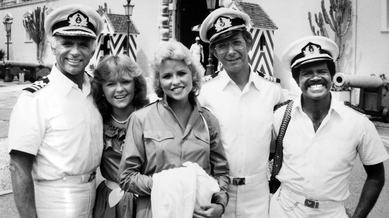 Gavin MacLeod, Jill Whelan, Lauren Tewes, Bernie Kopell, and Ted Lange smiling in a 1970s photo on set of 