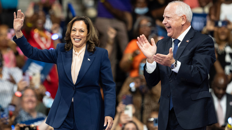 Tim Walz clapping and smiling while Kamala Harris waves to the crowd