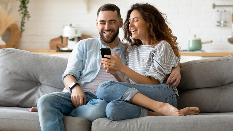 A couple laughs on the couch at their phone