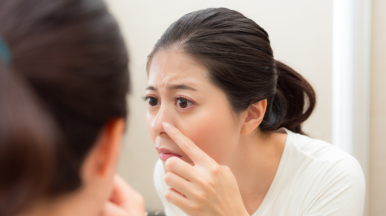 Worried lady touching her nose while looking at mirror