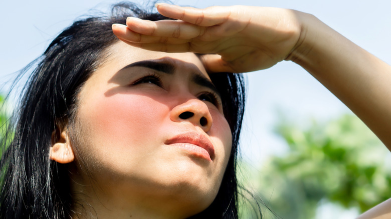 woman staring at the sun squinting with hand over eyes