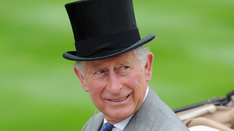 King Charles III smiling and wearing a top hat