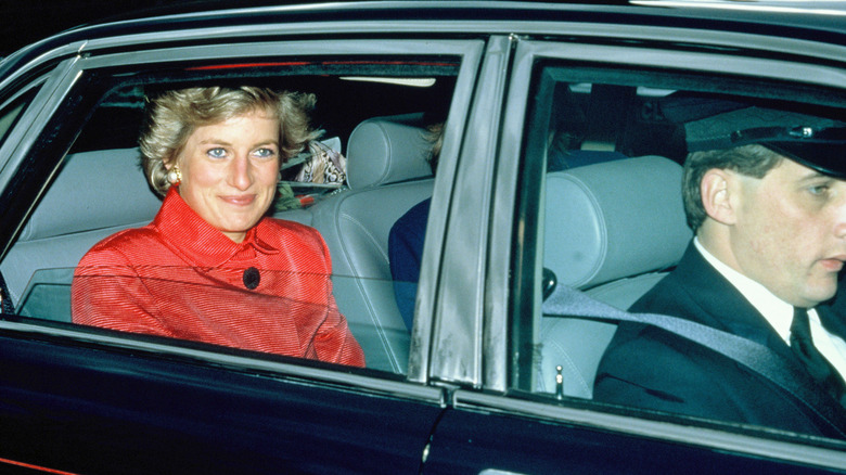 Princess Diana sitting in the back of a car in a red coat