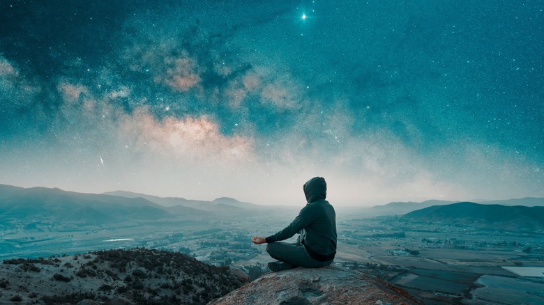 person meditating on top of a mountain under the stars