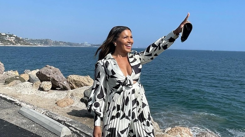 Page Turner standing next to sea and smiling as she points up to the sky
