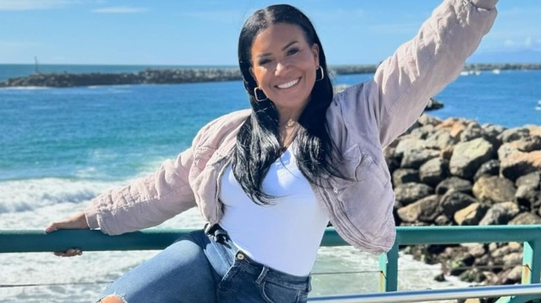 Page Turner smiling and raising her arm as she leans against railing near the beach