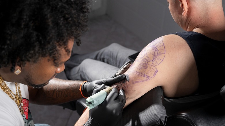 Tattoo artists works on client's upper arm