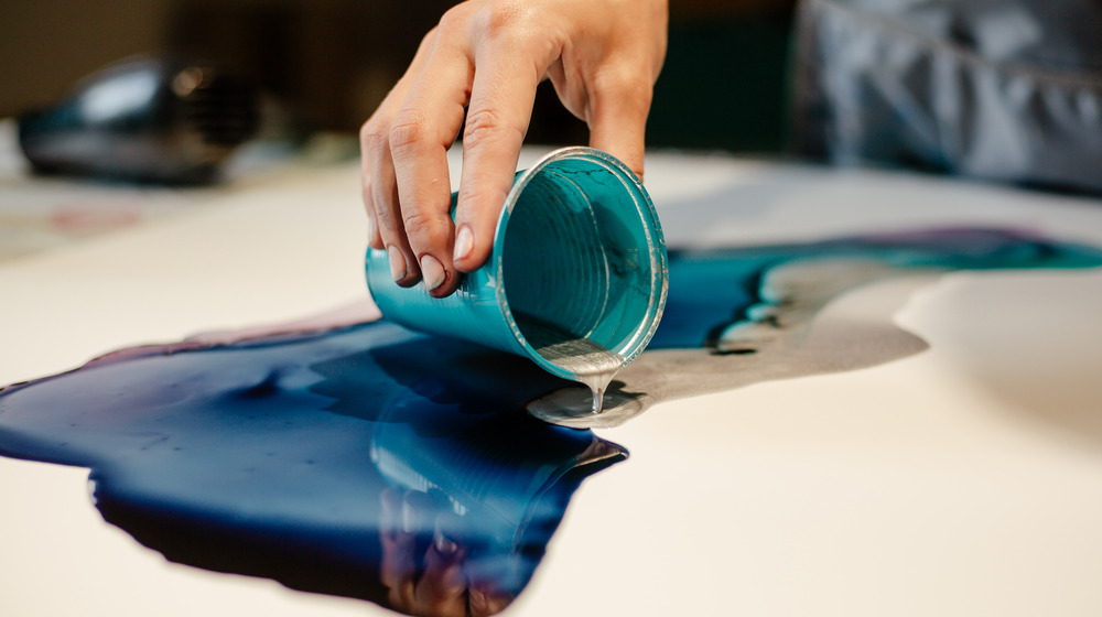 An artist pouring silver resin from a cup