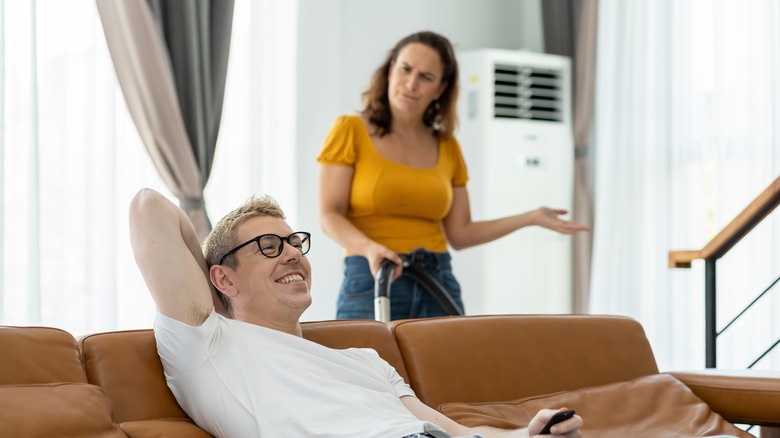 woman cleaning while man sits on couch 