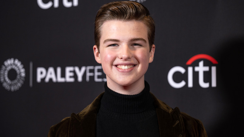Iain Armitage smiling while posing at an event in a black turtleneck and a dark brown velvet blazer
