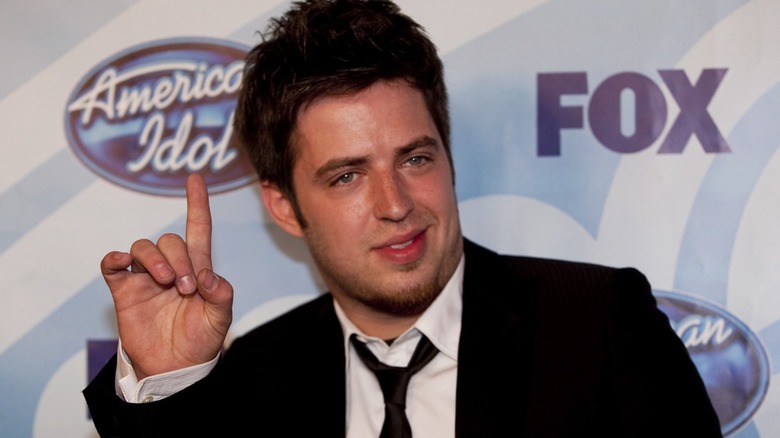Lee DeWyze on an American Idol step-and-repeat, pointing at the show's logo